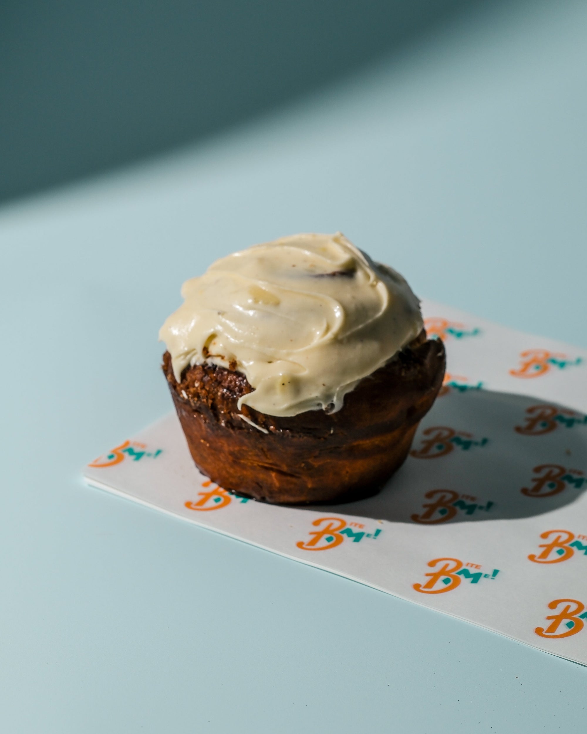 Cinnamon roll with cream cheese frosting on a branded napkin against a blue background
