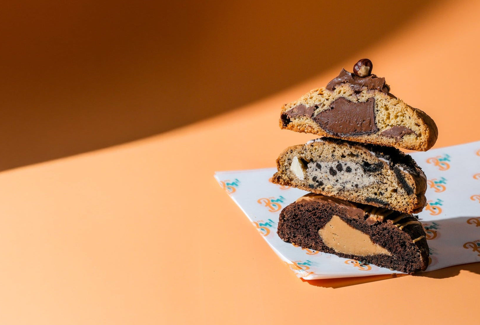 Stack of stuffed cookies, chocolate chip, oreo, peanut butter on a decorative paper napkin against an orange background